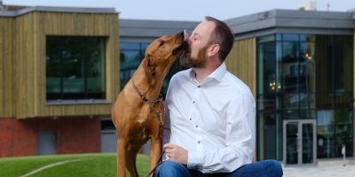 En hund slickar sin husse i ansiktet när de sitter på en gräskulle