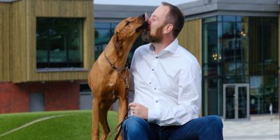 En hund slickar sin husse i ansiktet när de sitter på en gräskulle