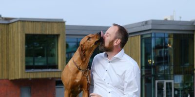 En hund slickar sin husse i ansiktet när de sitter på en gräskulle