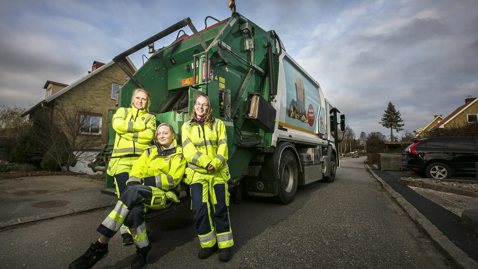 Tre tjejer står bakom en sopbil