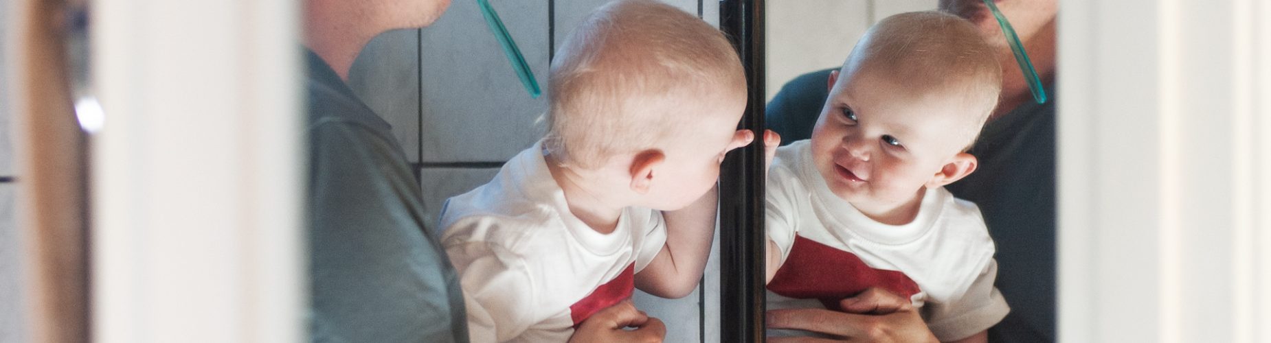 Pappa och bebis borstar tänderna och tittar sig i spegeln