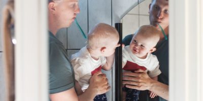 Pappa och bebis borstar tänderna och tittar sig i spegeln
