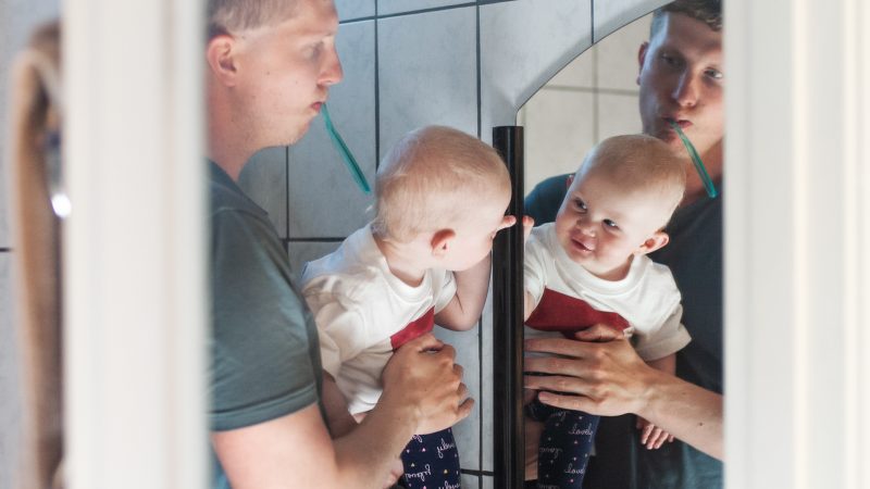 Pappa och bebis borstar tänderna och tittar sig i spegeln