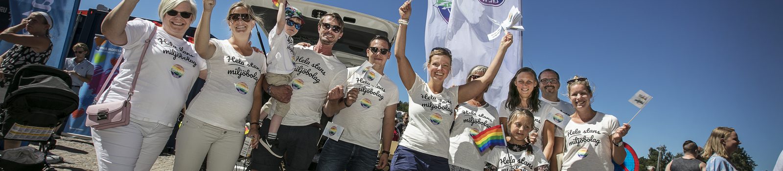 Ett glatt gäng med viftande prideflaggor i ett soligt Trollhättan