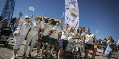 Ett glatt gäng med viftande prideflaggor i ett soligt Trollhättan