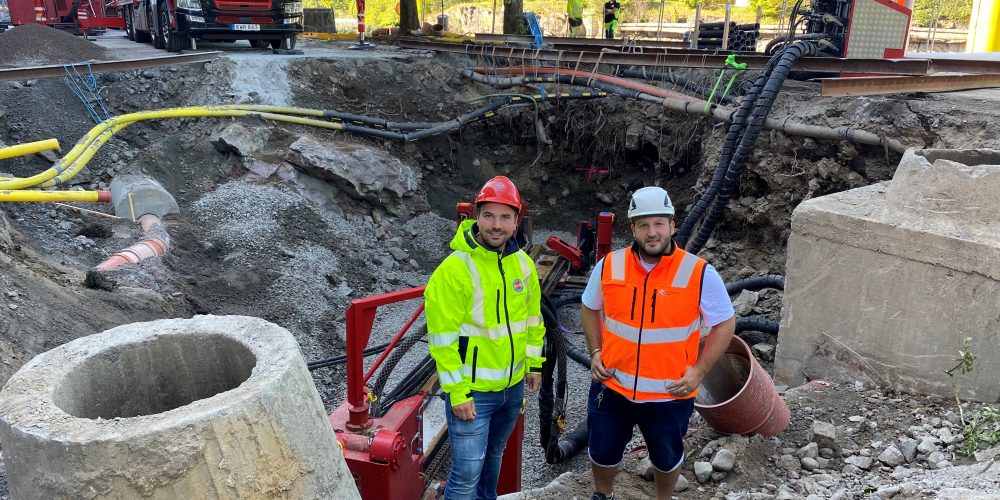 Två killar i byggkläder står vid ett stort schakt