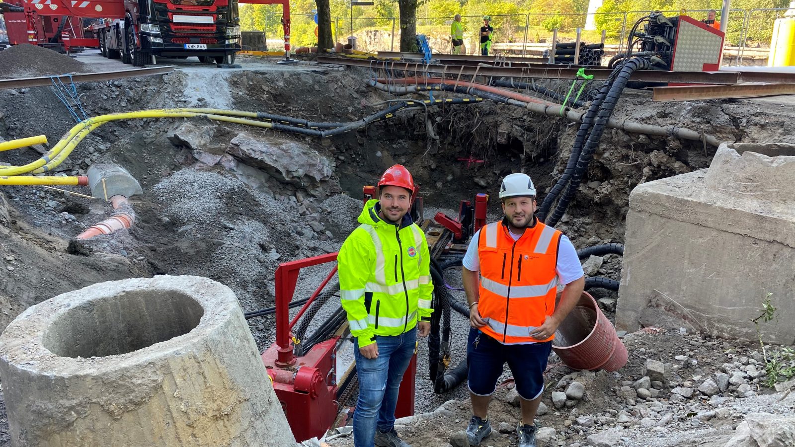 Två killar i byggkläder står vid ett stort schakt