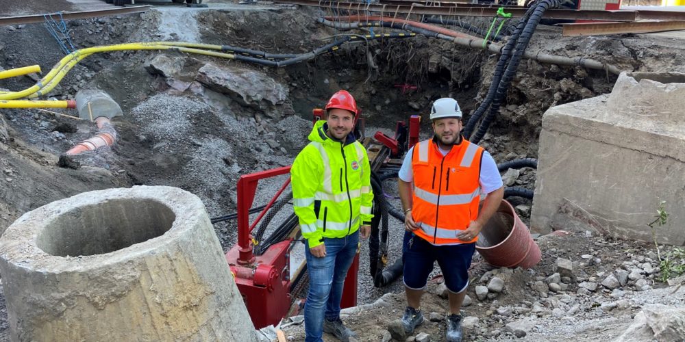 Två killar i byggkläder står vid ett stort schakt