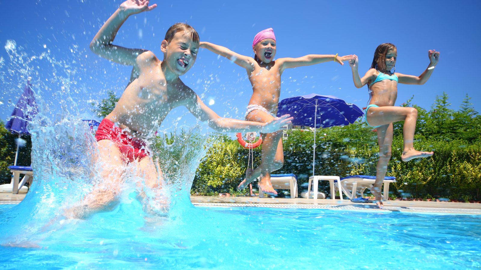 Två tjejer och en kille hoppar och leker i poolen
