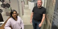 Tjej och kille står i kontorsmiljö och tittar in i kameran