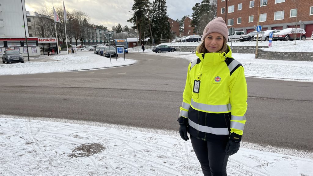 Tjej står ute i snön med varseljacka och mössa, vid en väg, tittar in i kameran.