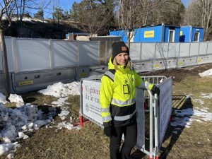 Tjej står vid kravallstaket framför byggarbetsplats